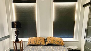 A bedroom with a bed, two windows, a lamp, and a small table. - Private Downtown Apartment in Red Cloud, in the heart of Willa Cather country (Red Cloud)