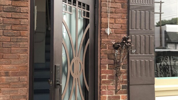 A black metal door with a decorative glass panel, a brick wall, and a window above the door. - Private Downtown Apartment in Red Cloud, in the heart of Willa Cather country (Red Cloud)