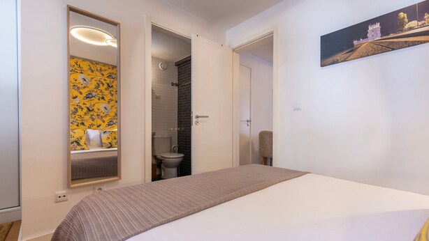Une chambre avec un lit, une salle de bain avec des toilettes et une douche, et un miroir devant un papier peint à motifs floraux.