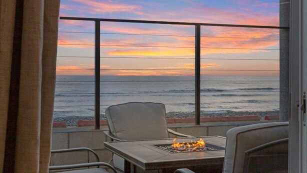 Un balcón con mesa y sillas, con vista al océano durante el atardecer.