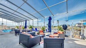 A covered outdoor lounge area with wicker furniture, umbrellas, and a pool in the background. - Paradise on the water w/ a pool & great fishing! (Saint James City)