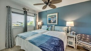 A bedroom with a bed, two bedside tables, a ceiling fan, a window with curtains, and a wall-mounted picture. - Paradise on the water w/ a pool & great fishing! (Saint James City)