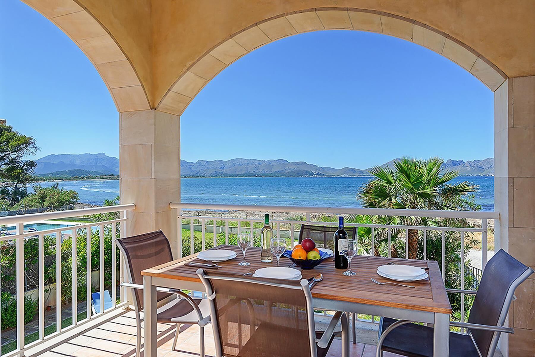 Ein Balkon mit Tisch für zwei Personen, mit Blick auf ein Gewässer und Berge.