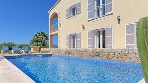 Una piscina con un muro in pietra e un edificio con diverse finestre e persiane.