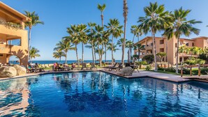 A swimming pool with lounge chairs and palm trees, surrounded by buildings with balconies overlooking the ocean. - Newly Remodeled, Great Views, Beachfront!  (San José del Cabo)