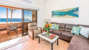 A living room with a view of the beach, a ceiling fan, a painting, and a coffee table with flowers. - Newly Remodeled, Great Views, Beachfront!  (San José del Cabo)