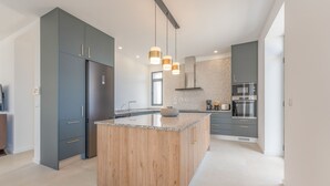 Cozinha moderna com ilha central, armários escuros e eletrodomésticos de aço inoxidável.