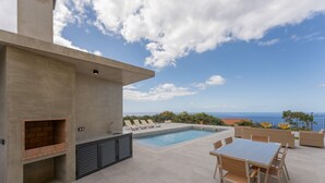 Uma área de piscina no terraço com churrasqueira, espreguiçadeiras e uma mesa de jantar.