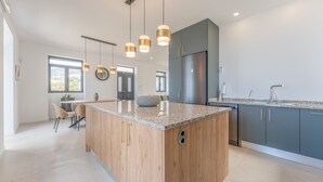 Cozinha moderna com ilha central, iluminação pendente e vista para a área de refeições.