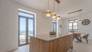 Cozinha moderna com uma ilha grande, luminárias pendentes e uma área de refeições com cadeiras.