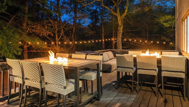 Une terrasse extérieure dotée d’un foyer, de sièges et de guirlandes lumineuses.