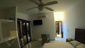 A hotel room with a bed, a chair, a TV, a ceiling fan, and a door leading to another room. - Casa Bugambilia-Santa Cruz Pool & walk to Beach! (Avienda)