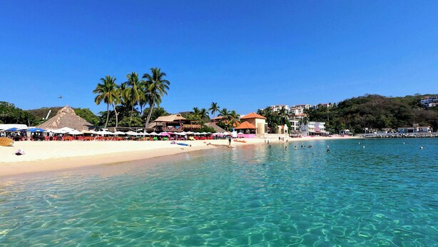A beach with clear turquoise water, palm trees, and beachside buildings. - Casa Bugambilia-Santa Cruz Pool & walk to Beach! (Avienda)