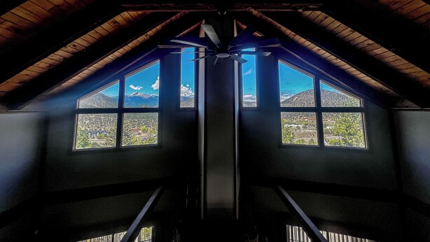 Ein Zimmer mit schrägen Wänden und großen Fenstern, das einen Blick auf eine gebirgige Landschaft bietet.