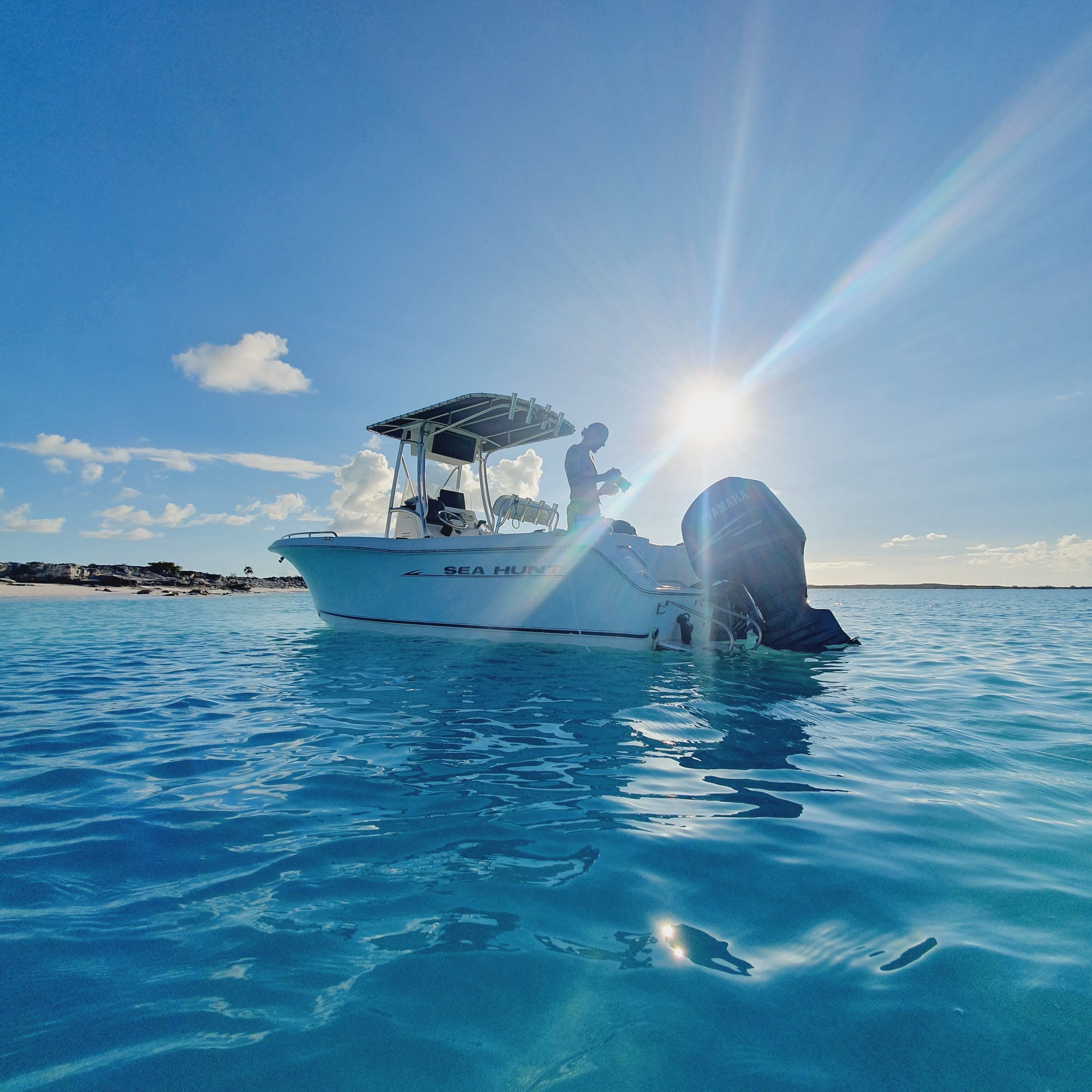 Un bateau nommé «SEA HUNTER» navigue sur une eau d’un bleu limpide, avec un soleil éclatant en arrière-plan.