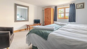Ein Hotelzimmer mit einem Bett, einem Holzschrank, einem Schreibtisch mit Fernseher, einem Sessel und einem großen Spiegel an der Wand.