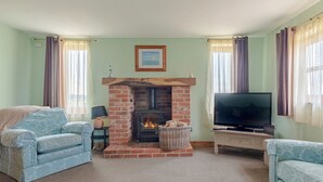 Ein Wohnzimmer mit Kamin aus Ziegelsteinen, zwei Sofas, einem Fernseher und einem gerahmten Bild an der Wand.