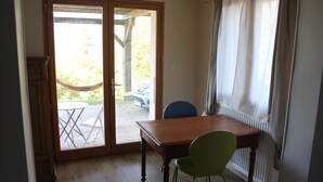 Una stanza con un tavolo di legno e una sedia verde, con una porta vetrata scorrevole che dà su un'area esterna con un'amaca e un'auto blu.