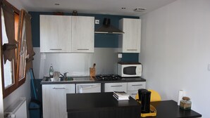 Cucina compatta con mobili bianchi, microonde, fornello e un piccolo spazio pranzo con tavolo e sedia.