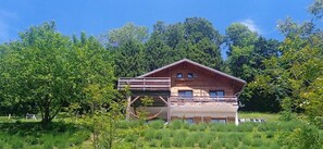 A wooden cabin with a balcony, surrounded by lush greenery and trees. - 1-Bedroom Apartment in Bouvante (Bouvante)