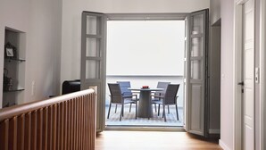 En modern inredning med trägolv, utsikt över en balkong med bord och stolar och en stor, öppen dörr.