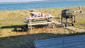 A picnic setup with a grill and table by a lake. - Beach Bliss (Boylston)