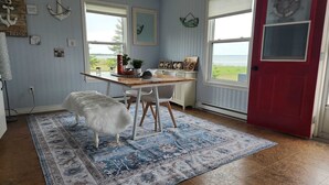 A room with a wooden desk, white chairs, a rug, and a red door. - Beach Bliss (Boylston)
