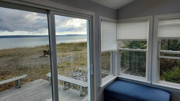 A room with large windows overlooking a beach and water. - Beach Bliss (Boylston)