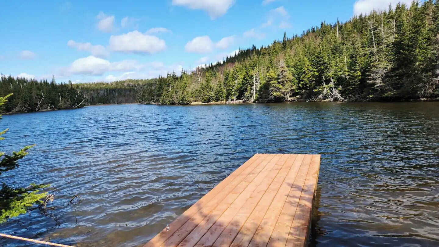 Un muelle de madera que se adentra en un lago tranquilo rodeado de un bosque frondoso.