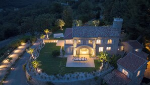 A large stone house with a spacious patio, surrounded by a well-maintained garden and a stone wall.