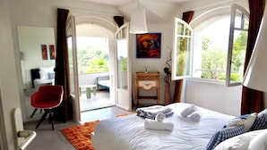 A hotel room with a bed, a desk, a chair, a small table, and a painting.