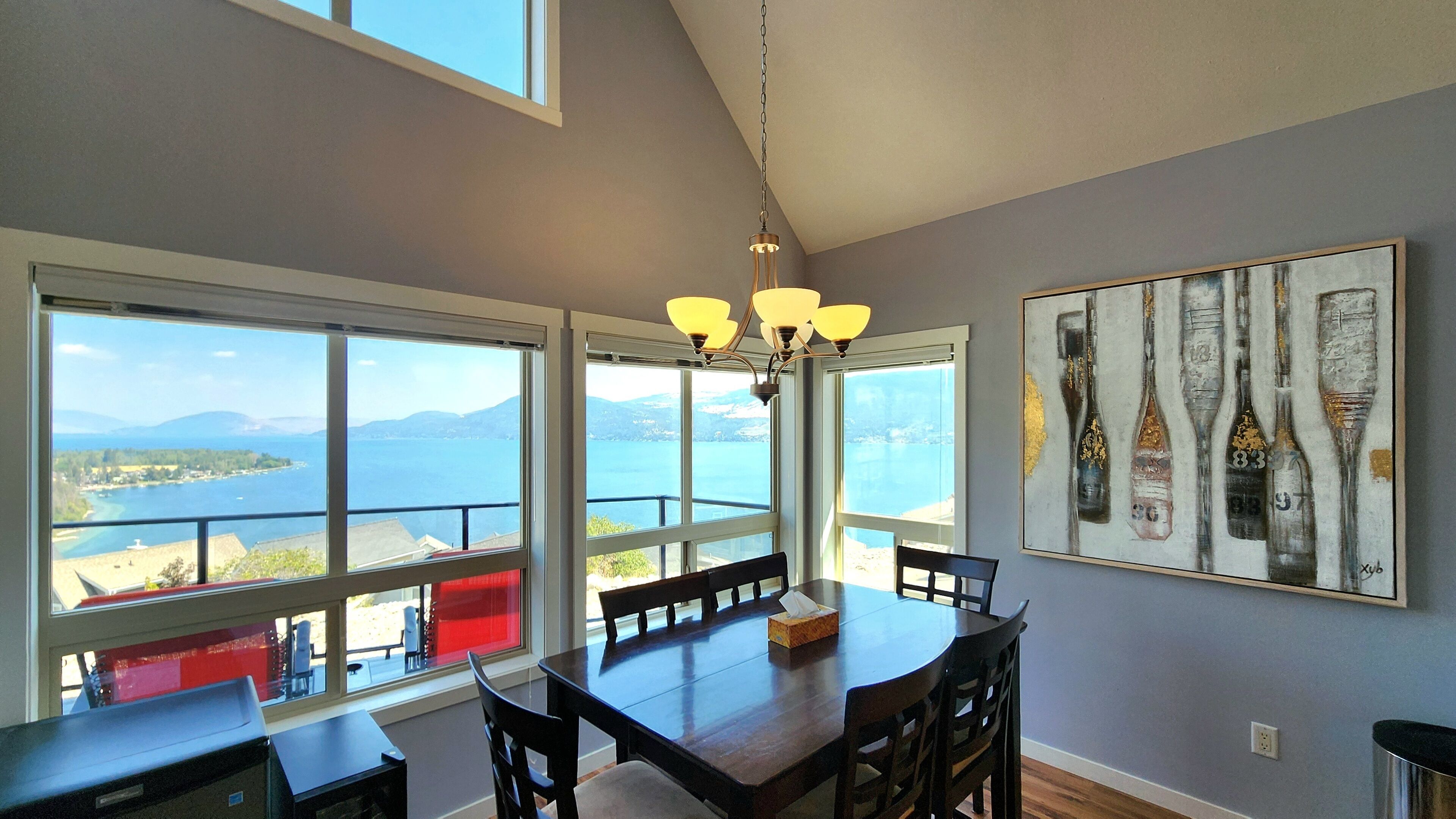 A dining area with a view of the sea and mountains, a chandelier, and a painting on the wall.