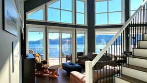 Ampla sala de estar com vista para o mar, uma escadaria e um espaço de jantar com mesa e cadeiras.