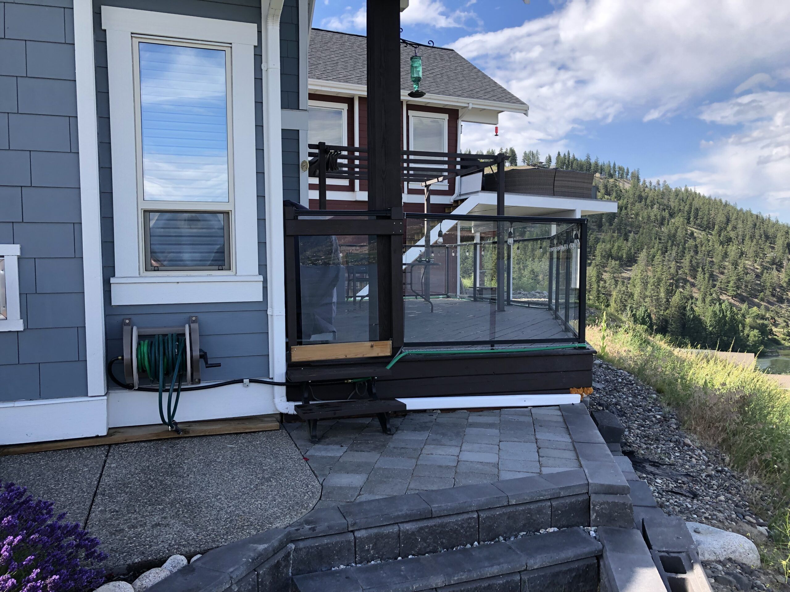Ein modernes Haus mit einer Glasdeckfläche, einer Holztreppe und Blick auf einen bewaldeten Hang.