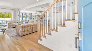 A spacious living area with a staircase, a dining area, and a view through large windows. - Popponesset-3-bedrooms, 3.5 baths, sleeps 6, A/C, Pool, Firepit (Mashpee)