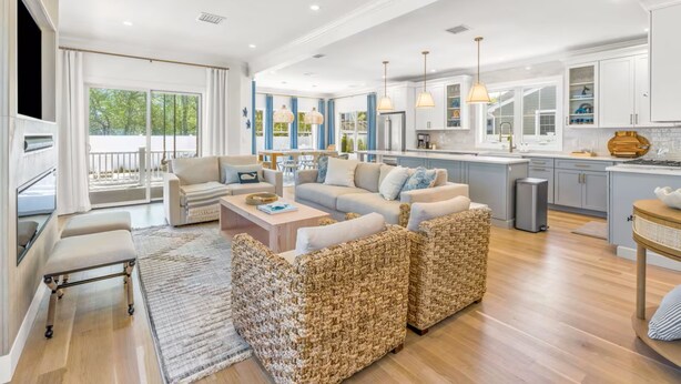 A spacious living area with a sofa set, a coffee table, and a TV. There is a kitchen area with modern appliances and pendant lighting. - Popponesset-3-bedrooms, 3.5 baths, sleeps 6, A/C, Pool, Firepit (Mashpee)