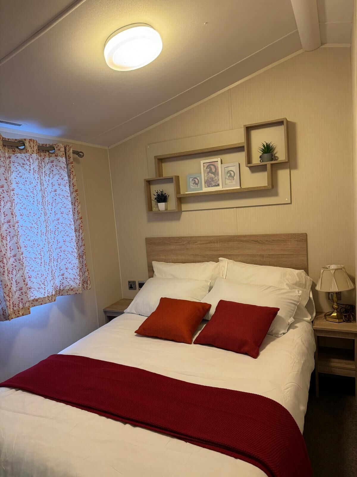 Una cama bien hecha con ropa de cama blanca y roja, un cabecero de madera y una mesita de noche con una lámpara.