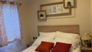 A neatly made bed with white and red bedding, a wooden headboard, and a nightstand with a lamp.