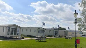A row of mobile homes with a grassy lawn and picnic tables. - Modern & Blissful Beach Holiday Park Home in Essex (Harwich)