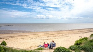 A beach with people sitting on chairs, a clear sky, and a calm sea. - Modern & Blissful Beach Holiday Park Home in Essex (Harwich)