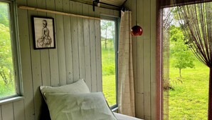 Ein Schlafzimmer mit Bett, Fenster, einem Bild an der Wand und Blick auf Grünfläche.