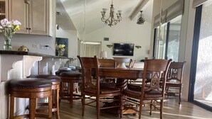 Zona pranzo con tavolo e sedie in legno, un lampadario e un'ampia finestra che lascia entrare luce naturale.