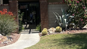 Un ingresso di un edificio con un portico coperto, un vialetto che conduce alla porta e diverse piante e cactus nella sistemazione del giardino.