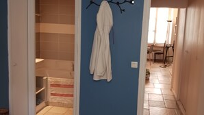 Un couloir avec un mur bleu, une robe blanche suspendue à une décoration en forme de branche, et un sol carrelé.