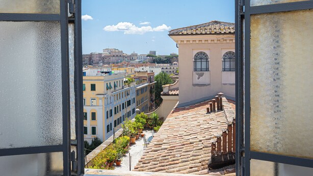 A view through a window with frost patterns, overlooking a street with terracotta-tiled buildings and a clear blue sky. - Amazing Penthouse Prati (Roma)