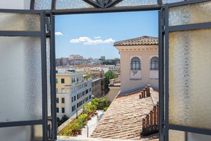 A view through a window with frost patterns, overlooking a street with terracotta-tiled buildings and a clear blue sky. - Amazing Penthouse Prati (Roma)