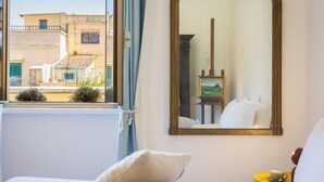 A hotel room with a bed, a bedside table with a cup, a large mirror, and a window with curtains. - Amazing Penthouse Prati (Roma)
