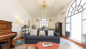 A living room with a piano, a sofa, a coffee table, and a chandelier. - Amazing Penthouse Prati (Roma)