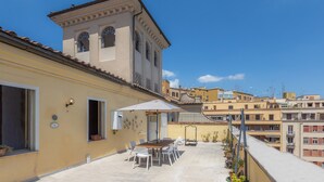 A rooftop terrace with a dining table and chairs, a small building with arched windows, and a clear blue sky. - Amazing Penthouse Prati (Roma)