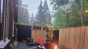 En trädgård med en eldstad, röda stolar och ljusslingor.